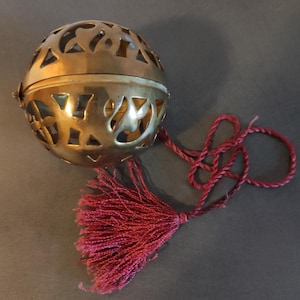 May include: A gold metal sphere with intricate cut-out designs and a red tassel attached to a cord.