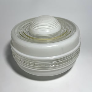 May include: A round, white glass light fixture shade featuring a stepped, dome-shaped center and a clear, textured band with a grid pattern around the middle. The glass has a smooth, opaque finish with concentric rings surrounding the central dome.