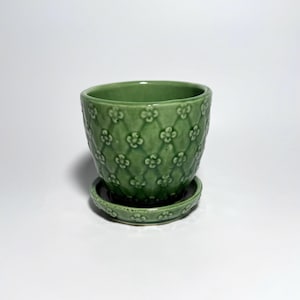 May include: A sage green ceramic plant pot with a matching saucer. The exterior of the pot features a raised, embossed diamond lattice pattern with small four-petaled flowers centered within each diamond shape, finished in a glossy glaze.