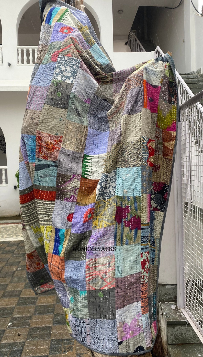 May include: A patchwork quilt with a variety of colors and patterns, including floral, geometric, and abstract designs. The quilt is made of recycled saris and is hand-stitched. The quilt is hanging on a wall and has the text "WOMENKNACKS" printed on it.