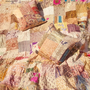 May include: A patchwork quilt with a cream background and colorful floral patterns. Two decorative pillows are placed on top of the quilt. The pillows are also patchwork and have a cream background with colorful floral patterns.