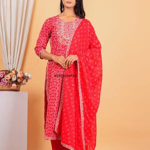 May include: A red and white printed kurta with a matching palazzo pant and dupatta. The kurta has a round neckline and three-quarter sleeves. The dupatta has a gold border.