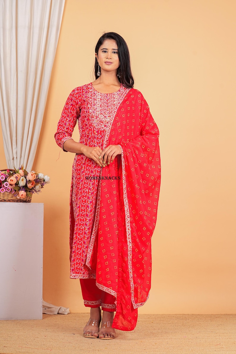 May include: A red and white printed kurta with a matching palazzo pant and dupatta. The kurta has a round neckline and three-quarter sleeves. The dupatta has a gold border.