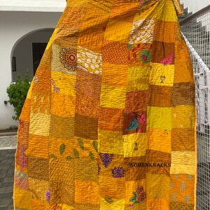 Pu&ograve; includere: Una trapunta patchwork rettangolare composta da quadrati di tessuto in varie tonalit&agrave; di giallo e arancione. Il tessuto presenta motivi diversi, tra cui disegni floreali, forme geometriche e piccole stampe di animali, uniti da visibili cuciture bianche.