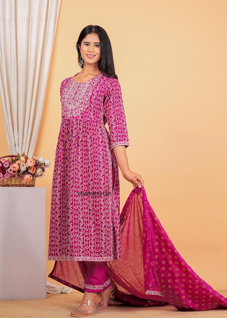 May include: A magenta and white patterned kurta with a matching dupatta and pants. The kurta has a round neckline and three-quarter sleeves. The dupatta is sheer and has a floral pattern. The pants are slim-fitting and have a straight leg.