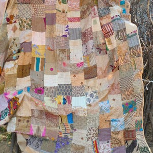 Op de afbeelding: Een patchworkquilt met een verscheidenheid aan stofpatronen en kleuren, waaronder beige, bruin, roze en blauw. De quilt is gemaakt van vierkanten en rechthoeken van verschillende maten en texturen. De tekst "WOMENKNACKS" is zichtbaar.