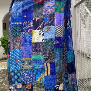 Pu&ograve; includere: Una trapunta patchwork caratterizzata da una variet&agrave; di quadrati di tessuto blu, verde acqua e viola con diversi motivi floreali, geometrici e paisley. Il tessuto &egrave; realizzato con impunture bianche visibili e il testo WOMEN KNACKS.