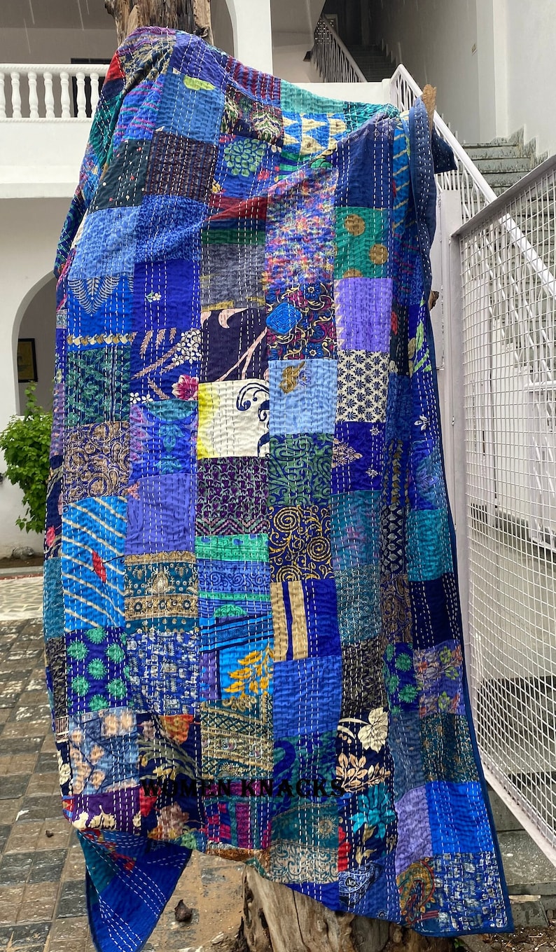 Pu&ograve; includere: Una trapunta patchwork caratterizzata da una variet&agrave; di quadrati di tessuto blu, verde acqua e viola con diversi motivi floreali, geometrici e paisley. Il tessuto &egrave; realizzato con impunture bianche visibili e il testo WOMEN KNACKS.