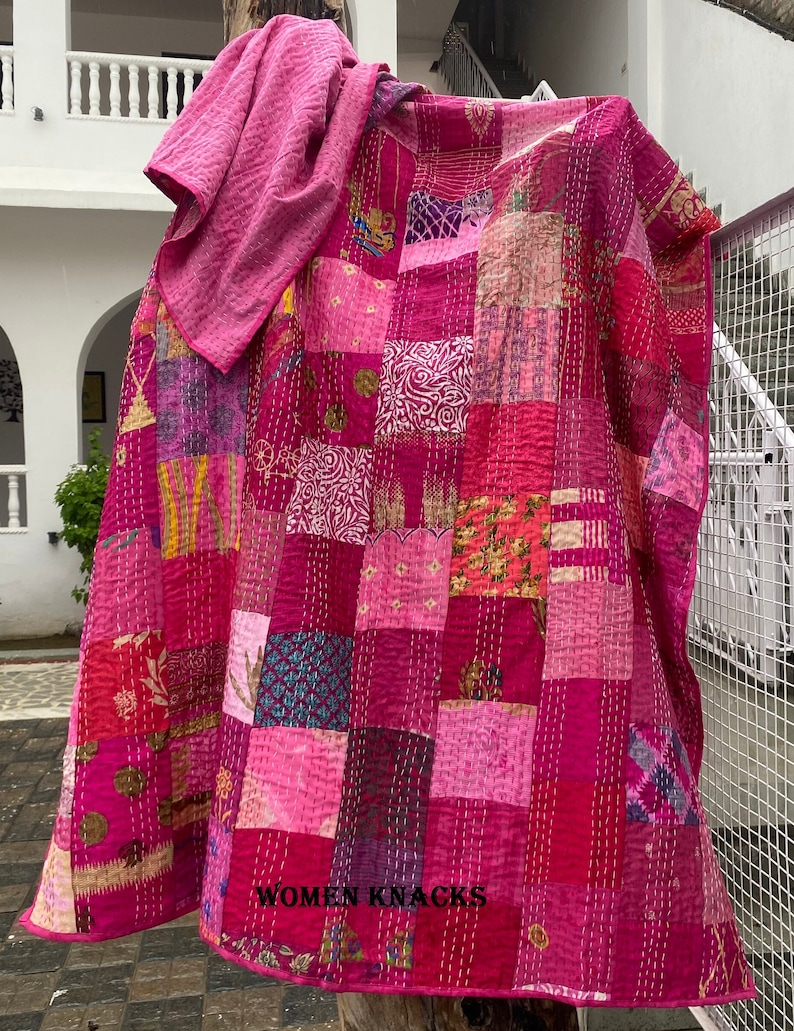 Pu&ograve; includere: Una trapunta patchwork composta da quadrati di tessuto in varie tonalit&agrave; di rosa e magenta con cuciture kantha bianche. Il tessuto presenta diversi motivi, tra cui disegni floreali, geometrici e astratti, con il testo WOMEN KNACKS.