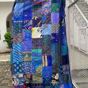 May include: A blue kantha quilt with a patchwork design featuring various shades of blue, green, purple, and gold. The quilt is made of recycled saris and is hand-stitched.