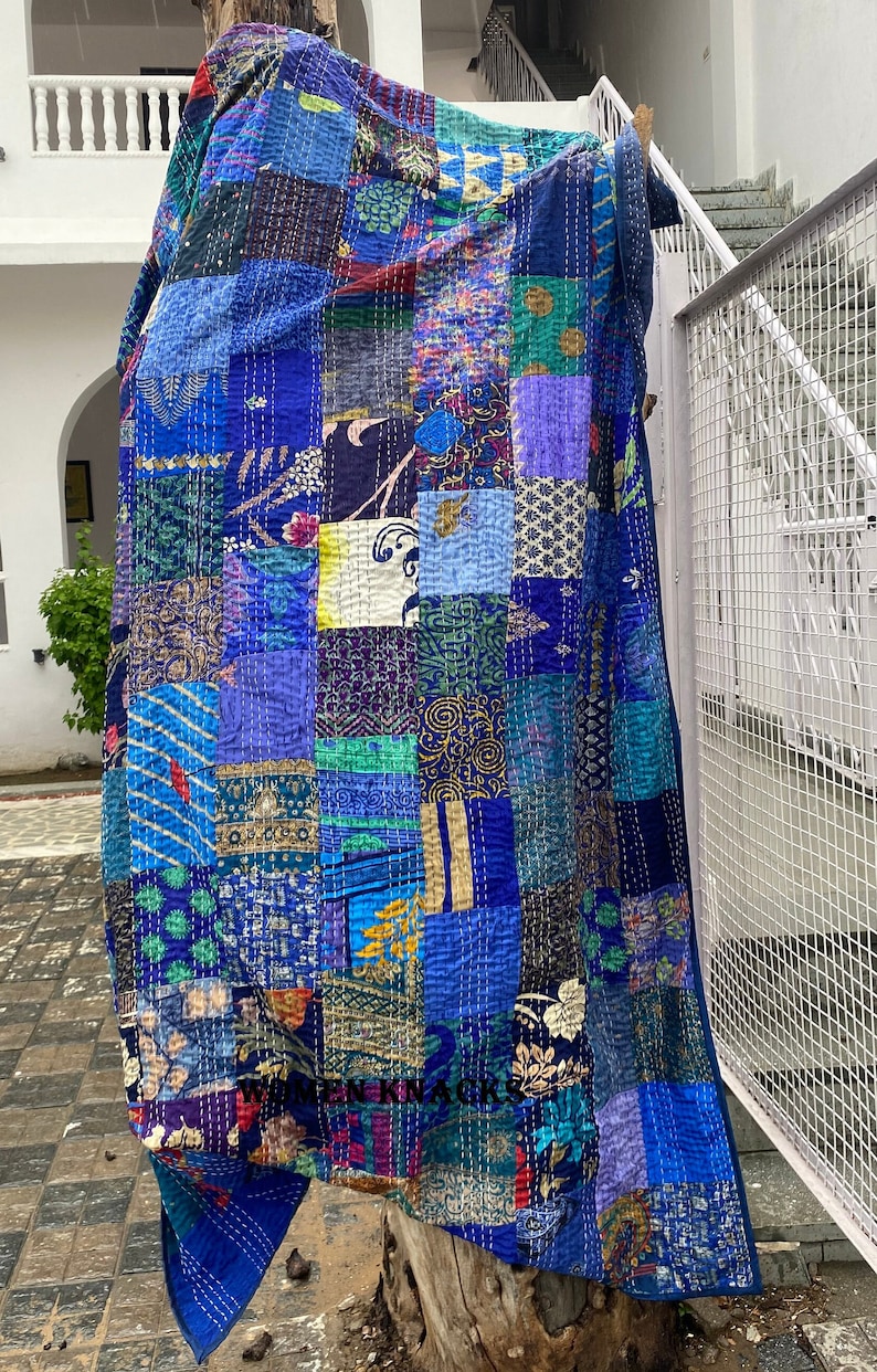 May include: A blue kantha quilt with a patchwork design featuring various shades of blue, green, purple, and gold. The quilt is made of recycled saris and is hand-stitched.