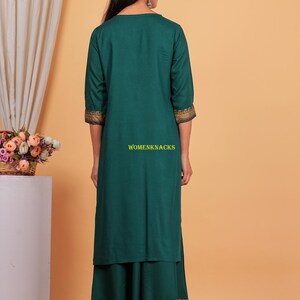 May include: A teal green long kurta with gold trim on the sleeves and bottom hem. The kurta is paired with a matching teal green skirt with gold trim. The skirt has a layered design.