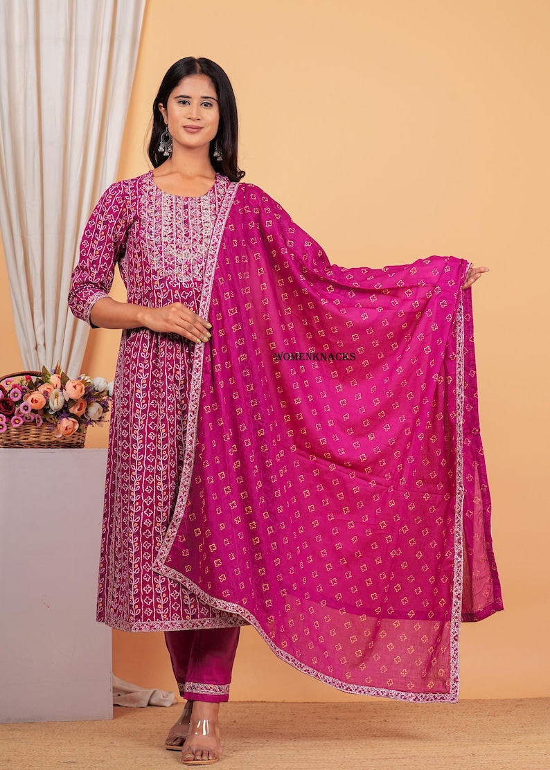 May include: A magenta kurta with a white floral print and a matching magenta palazzo pant. The kurta has a white embroidered neckline and the set includes a magenta dupatta with a white border and a small square print.