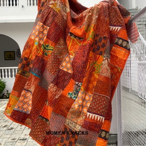 May include: A large, orange and brown patchwork quilt with intricate stitching. The quilt is made of various fabrics with floral and geometric patterns. The quilt is draped over a wooden post and has the text "WOMEN KNACKS" printed on the bottom right corner.