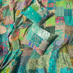 May include: A patchwork quilt with a variety of green, blue, and brown fabrics. The quilt is made of many different squares and rectangles, and it is decorated with a variety of patterns. Two matching pillow covers are included, also made of patchwork fabric.