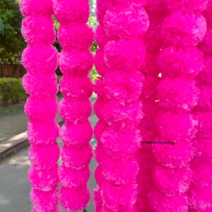K&ouml;nnte beinhalten: Eine Girlande aus leuchtend pinken Papierblumen, die an einer langen Schnur aneinandergereiht sind. Die Blumen sind aus zerknittertem Papier und haben eine flauschige Textur. Die Girlande ist perfekt, um jeder Gelegenheit einen Hauch von Farbe und Festlichkeit zu verleihen.