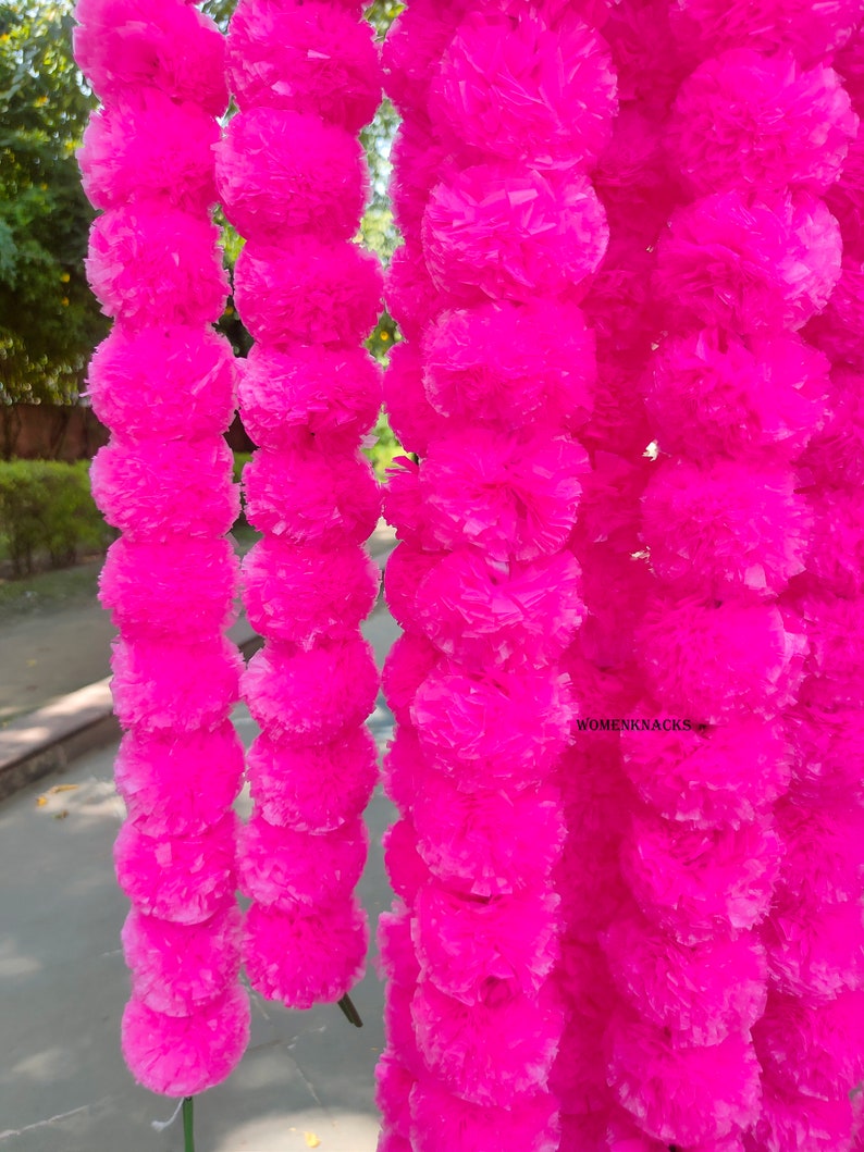 K&ouml;nnte beinhalten: Eine Girlande aus leuchtend pinken Papierblumen, die an einer langen Schnur aneinandergereiht sind. Die Blumen sind aus zerknittertem Papier und haben eine flauschige Textur. Die Girlande ist perfekt, um jeder Gelegenheit einen Hauch von Farbe und Festlichkeit zu verleihen.