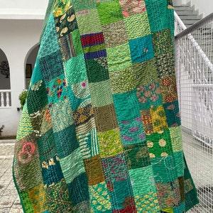 May include: A patchwork quilt made from a variety of green fabrics with different patterns. The quilt is folded and draped over a tree stump. The text "WOMEN KNACKS" is visible in the bottom right corner of the quilt.