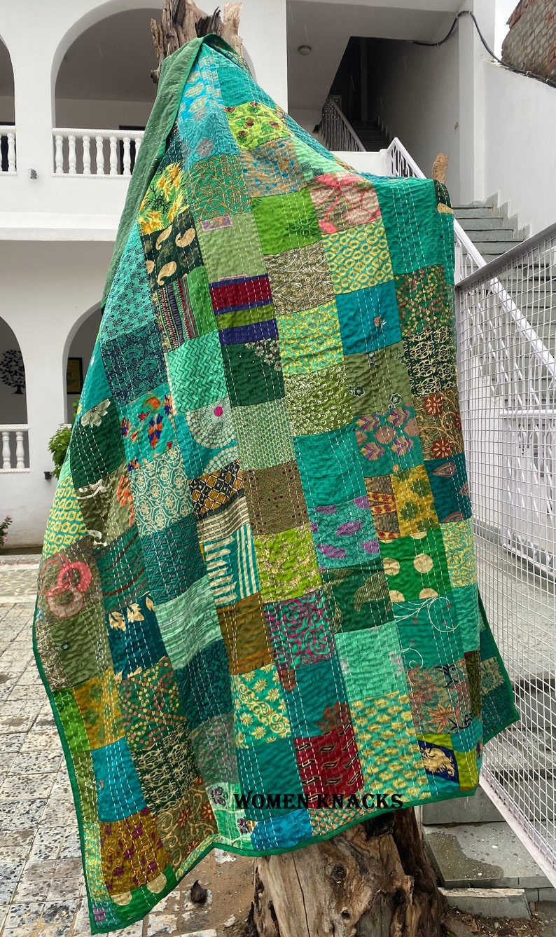 Pu&ograve; includere: Una trapunta patchwork composta da vari quadrati di tessuto nei toni del verde con motivi diversi, tra cui disegni floreali, paisley e geometrici. La trapunta &egrave; cucita con un filo bianco visibile e riporta il testo WOMEN KNACKS.