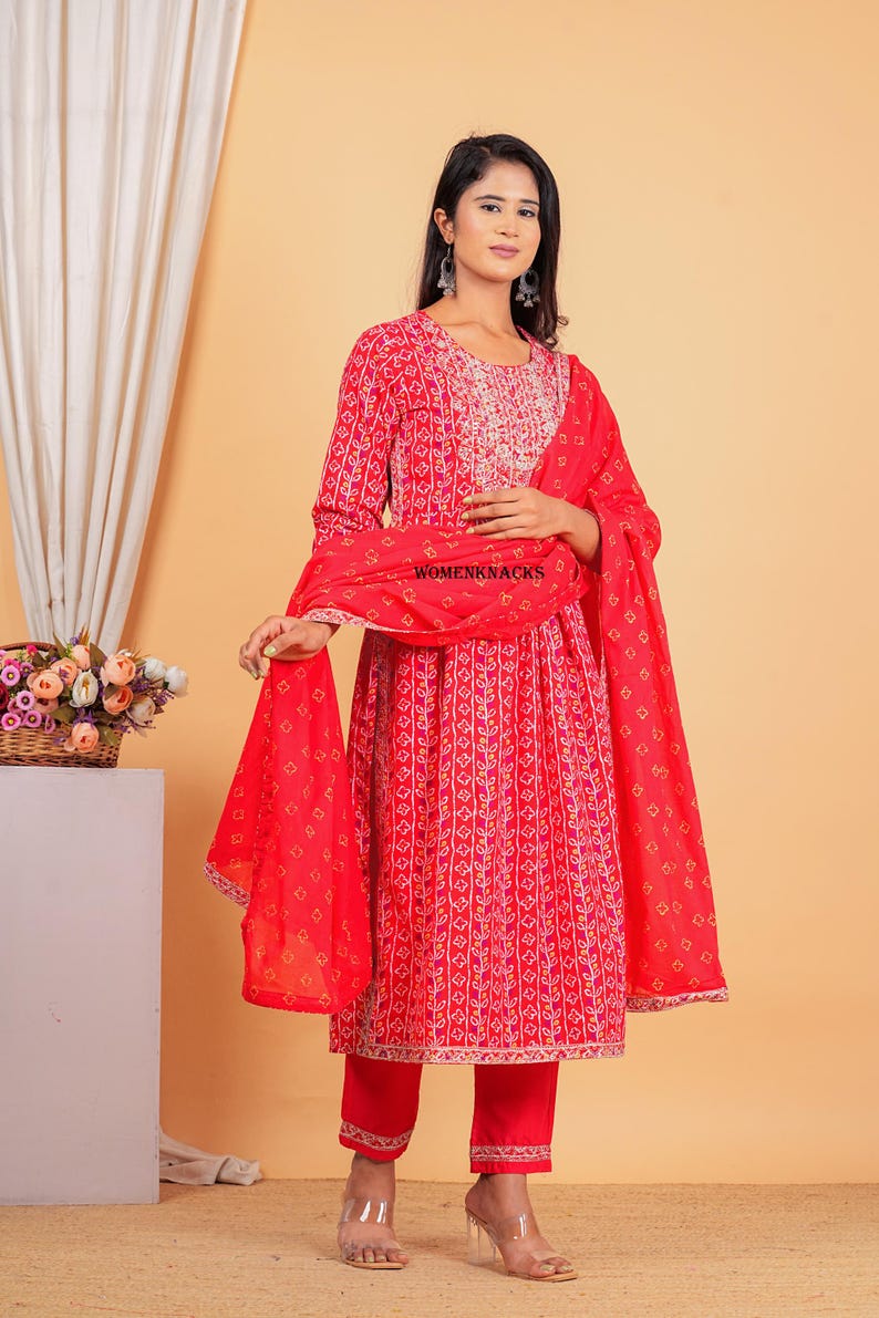 May include: A red and white printed kurta with a matching red palazzo pant and a red dupatta. The kurta has a round neckline and three-quarter sleeves. The dupatta has a floral print and a gold border. The outfit is perfect for a special occasion.