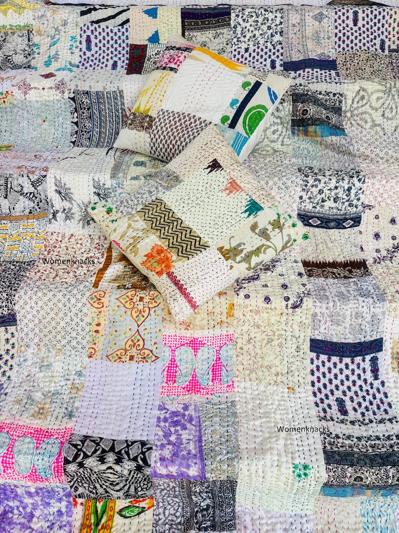 Pu&ograve; includere: Una trapunta patchwork e due cuscini quadrati abbinati con vari ritagli di tessuto stampato in bianco, rosa, blu, verde e nero. I pezzi di tessuto sono uniti da visibili impunture bianche e dal testo Womenknacks.