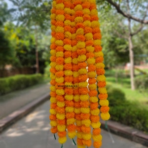 K&ouml;nnte beinhalten: Eine Girlande aus gelben und orangefarbenen Margeriten-Bl&uuml;tenkugeln, die aneinandergereiht sind und an einem Draht h&auml;ngen. Die Girlande ist etwa 90 cm lang und besteht aus k&uuml;nstlichen Blumen.