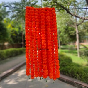 K&ouml;nnte beinhalten: Eine lange Girlande aus orangefarbenen Ringelblumen, die aneinandergereiht sind und an einem Draht h&auml;ngen. Die Girlande besteht aus k&uuml;nstlichen Blumen und ist perfekt f&uuml;r die Dekoration zu einem besonderen Anlass.