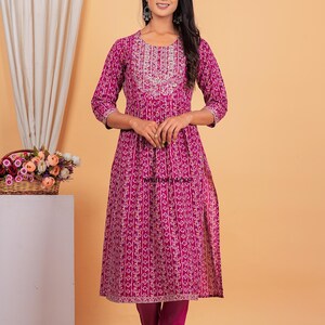 May include: A magenta printed kurta with a white embroidered neckline and matching pants. The kurta has a side slit and the pants have a gold trim.