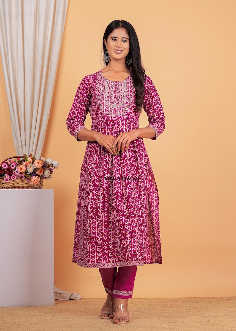 May include: A magenta printed kurta with a white embroidered neckline and matching pants. The kurta has a side slit and the pants have a gold trim.