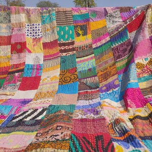 Puede incluir: Un edredón de patchwork vibrante con multitud de colores y patrones. El edredón está hecho de varios retazos de tela cosidos, creando un diseño único y texturizado. La paleta de colores incluye tonos de rosa, azul, amarillo y verde.