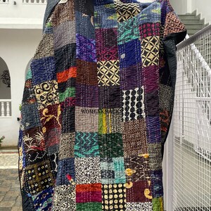 Pu&ograve; includere: Una trapunta patchwork caratterizzata da una variet&agrave; di pannelli rettangolari in tessuto con colori e motivi diversi, tra cui nero, blu, verde e oro. Il tessuto &egrave; cucito con un filo bianco visibile e riporta il testo WOMENK MAGIC.