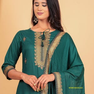 May include: A teal green kurta with gold embroidery and a matching dupatta. The kurta has a keyhole neckline with a tassel tie. The dupatta has a gold border with a red stripe.