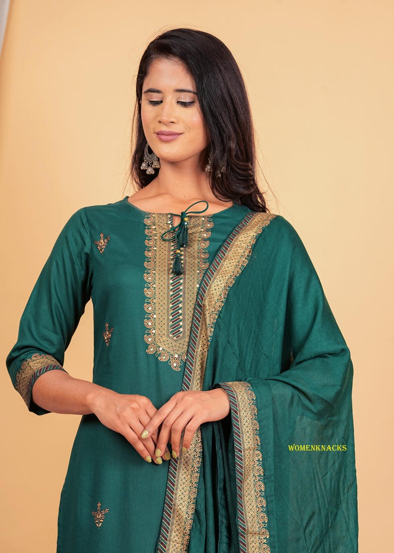 May include: A teal green kurta with gold embroidery and a matching dupatta. The kurta has a keyhole neckline with a tassel tie. The dupatta has a gold border with a red stripe.