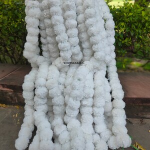 K&ouml;nnte beinhalten: Ein Stapel wei&szlig;er k&uuml;nstlicher Blumenkr&auml;nze, jede Girlande besteht aus kleinen wei&szlig;en Pompons. Die Kr&auml;nze sind mit gr&uuml;nem Garn zusammengebunden und bereit f&uuml;r die Dekoration.