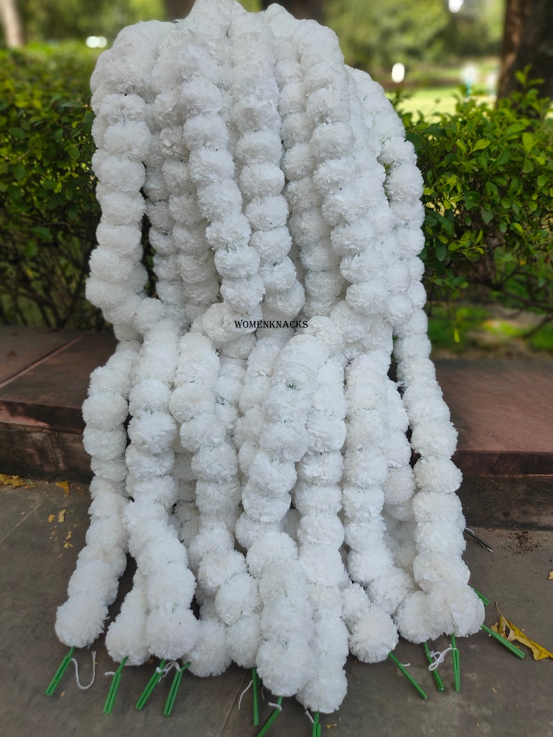 K&ouml;nnte beinhalten: Ein Stapel wei&szlig;er k&uuml;nstlicher Blumenkr&auml;nze, jede Girlande besteht aus kleinen wei&szlig;en Pompons. Die Kr&auml;nze sind mit gr&uuml;nem Garn zusammengebunden und bereit f&uuml;r die Dekoration.