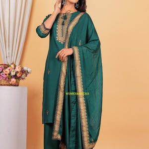 May include: A teal green kurta with gold embroidery and a matching dupatta. The kurta has a round neckline and three-quarter sleeves. The dupatta has a gold border and is draped over the shoulder.