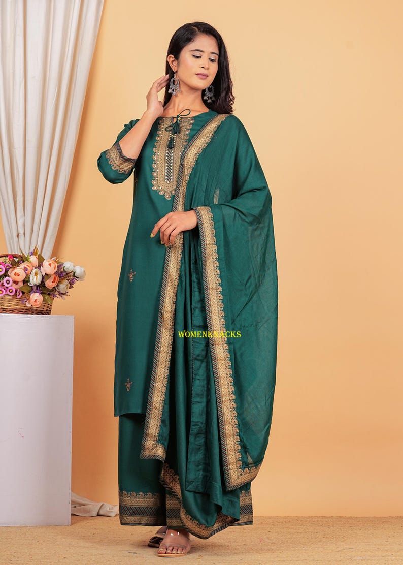 May include: A teal green kurta with gold embroidery and a matching dupatta. The kurta has a round neckline and three-quarter sleeves. The dupatta has a gold border and is draped over the shoulder.