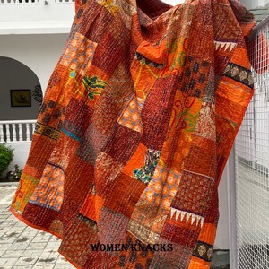 Pu&ograve; includere: Una trapunta patchwork composta da vari quadrati di tessuto arancioni, rossi e marroni con diversi motivi floreali, geometrici e paisley. Il tessuto &egrave; cucito con un filo bianco visibile e riporta la scritta WOMEN KNACKS.