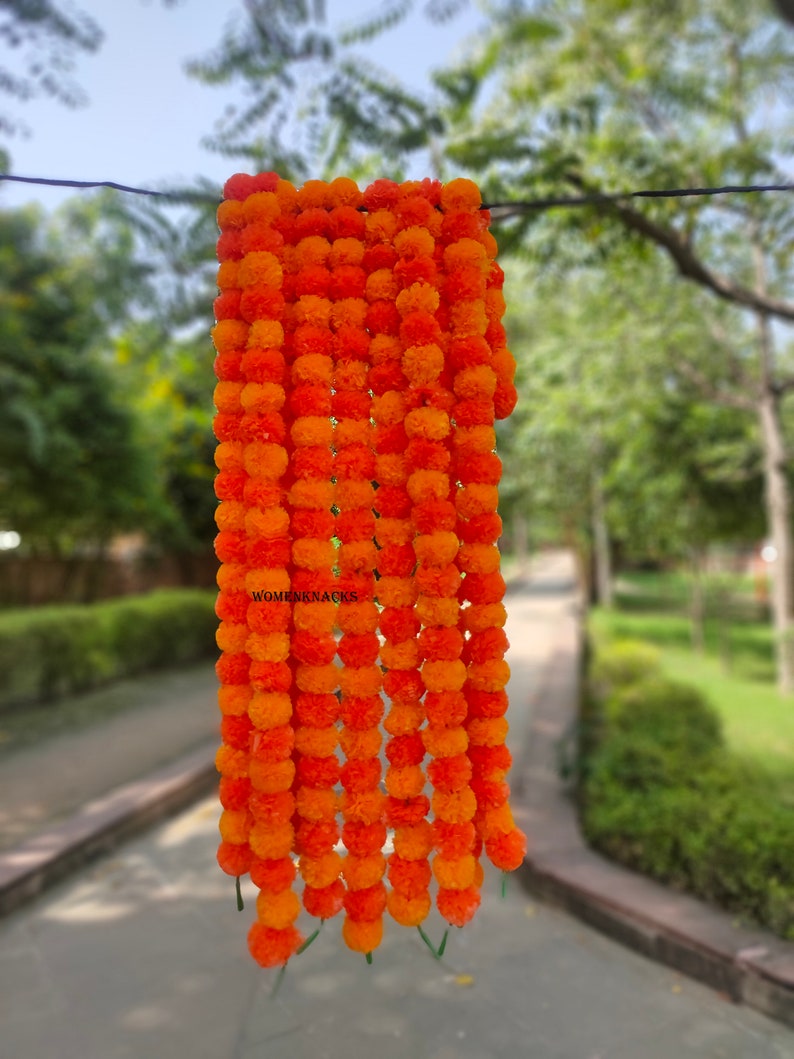 K&ouml;nnte beinhalten: Eine Girlande aus orangefarbenen und gelben Margeriten-Bl&uuml;tenkugeln, die an einem Draht h&auml;ngt. Die Girlande besteht aus k&uuml;nstlichen Blumen und ist perfekt f&uuml;r die Dekoration zu einem besonderen Anlass.