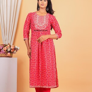 May include: A red and white printed kurta with a gold embroidered neckline and a matching pair of red pants. The kurta has a gathered waist and a long, flowing silhouette. The pants are slim-fitting and have a gold embroidered trim at the hem.
