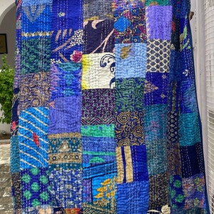 May include: A blue kantha quilt with a patchwork design. The quilt is made of various fabrics with different patterns and colours, including blue, green, purple, and gold. The quilt is hand-stitched with a running stitch.