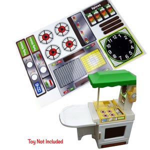 May include: A rectangular sticker sheet featuring kitchen appliance graphics including four stove burners, a clock, and control panels with the text "Party Kitchen" and "Spices". Below is a plastic toy kitchen set with a green roof.