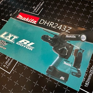 May include: A rectangular product card for a Makita DHR243Z rotary hammer drill. The teal and black card features the Makita logo, LXT 18V Lithium-Ion branding, and a BL Motor label. The drill is shown with a side handle and black grip.
