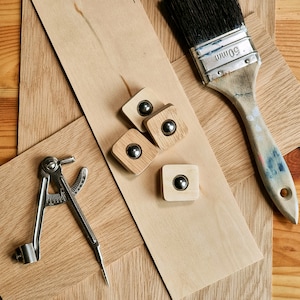 May include: An overhead shot of woodworking tools and materials. Includes a paintbrush, a compass, wooden squares with metal spheres, and various wood pieces. The paintbrush has a 50mm marking on the metal. The wood has a natural grain.
