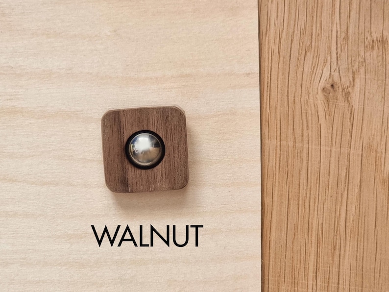May include: A square, walnut-colored wooden knob with a silver metal center. The word "WALNUT" is printed in black below the knob. The knob is set against a light wood grain background.