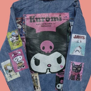 Può includere: Una giacca di jeans blu con varie toppe, tra cui una grande toppa di Kuromi con il testo "Born on October 31st Halloween", una toppa di Jaws e una toppa di Hello Kitty.