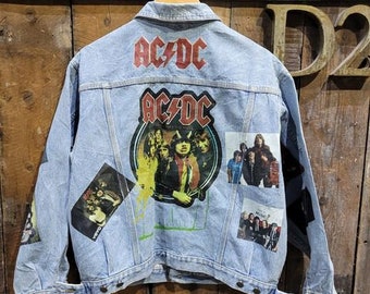 May include: A light blue denim jacket with patches featuring the band AC/DC. The patches include band members and the band's logo.