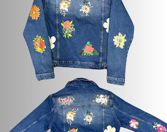 May include: A blue denim jacket with various floral patches, including roses, daisies, and other flower arrangements.