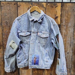 May include: A light blue denim jacket with patches, including a photo of a person playing a guitar. The jacket has a button closure and two pockets on the front.