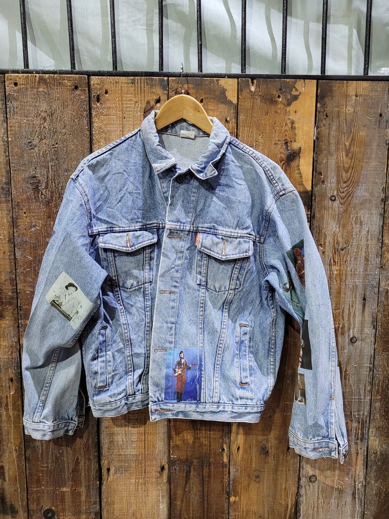 May include: A light blue denim jacket with patches, including a photo of a person playing a guitar. The jacket has a button closure and two pockets on the front.